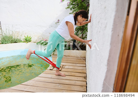 Woman exercising with resistance band outdoors near pool for fitness and strength training Woman exercising with resistance band outdoors near pool for fitness and strength training 118698494