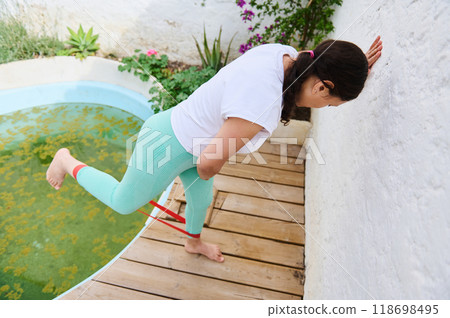 Woman exercising with resistance band by a poolside patio in comfortable outdoor setting for fitness and wellness Woman exercising with resistance band by a poolside patio in comfortable outdoor setting for fitness and wellness 118698495