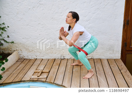 Woman practicing yoga on a wooden deck using resistance band for strength and balance training in outdoor setting 118698497