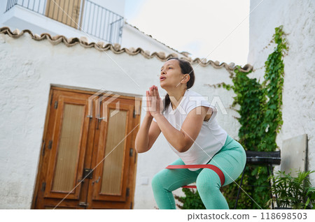Woman practicing outdoor workout with resistance band in courtyard, focused on fitness and wellness 118698503