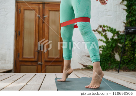 Woman practicing resistance band exercise on a wooden deck with a red fitness band outdoors 118698506