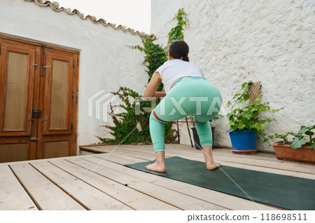 Woman exercising with resistance band on outdoor wooden deck, focusing on fitness and strength training in a serene garden setting 118698511