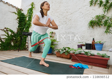 Woman practicing yoga on a wooden deck in peaceful outdoor setting with lush plants, embodying fitness and mindfulness with balance and tranquility 118698512