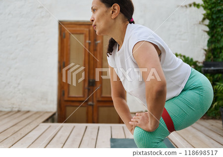 Middle-aged woman practicing yoga exercises outdoors on a wooden deck for physical fitness and mental well-being 118698517
