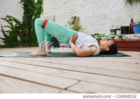 Woman practicing yoga outdoors, performing bridge pose for fitness and relaxation in a serene garden environment. Woman practicing yoga outdoors, performing bridge pose for fitness and relaxation in a serene garden environment. 118698532