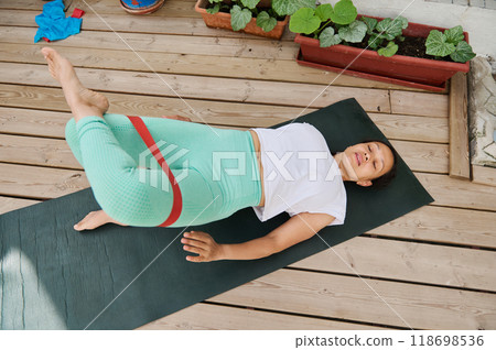 Woman practicing home workout with resistance band on yoga mat outdoors on wooden deck Woman practicing home workout with resistance band on yoga mat outdoors on wooden deck 118698536