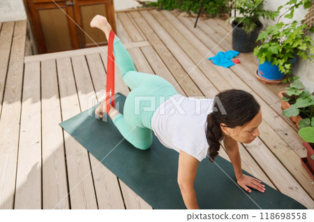 Woman practicing yoga with resistance band on outdoor deck for strength and flexibility Woman practicing yoga with resistance band on outdoor deck for strength and flexibility 118698558