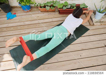 Woman practicing outdoor resistance band workout on yoga mat in garden setting for fitness and relaxation 118698564