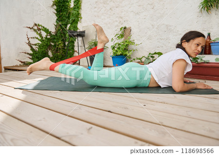 Woman practicing outdoor fitness with resistance band on yoga mat in peaceful garden setting 118698566