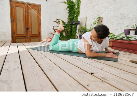 Woman practicing yoga outdoors on wooden deck in peaceful setting, wearing casual workout attire and engaging in relaxation and fitness Woman practicing yoga outdoors on wooden deck in peaceful setting, wearing casual workout attire and engaging in relaxation and fitness 118698567