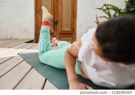 Woman in activewear exercising outdoors with resistance band on wooden deck for healthy lifestyle and fitness Woman in activewear exercising outdoors with resistance band on wooden deck for healthy lifestyle and fitness 118698569