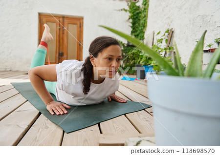 Woman practicing yoga on wooden deck outdoors focusing on exercise and relaxation amidst greenery Woman practicing yoga on wooden deck outdoors focusing on exercise and relaxation amidst greenery 118698570