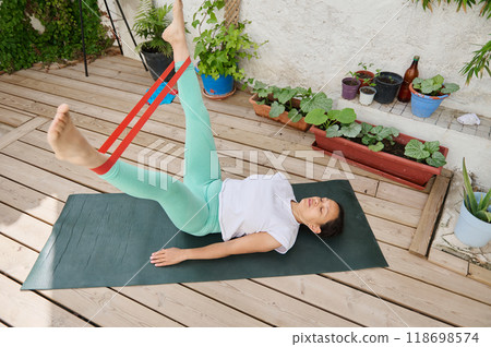 Woman practicing outdoor exercise with resistance band on yoga mat in garden setting Woman practicing outdoor exercise with resistance band on yoga mat in garden setting 118698574