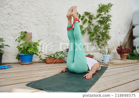 Woman practicing yoga on a wooden deck surrounded by potted plants in a serene outdoor setting 118698575