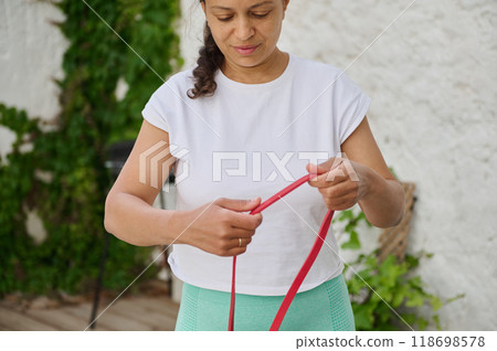 Woman preparing for workout with resistance band outdoors in a green garden setting for a healthy lifestyle and fitness routine 118698578