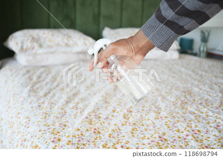 Using a hand spray, we are freshening up the bedding, which is on a floral quilt, in a cozy bedroom 118698794