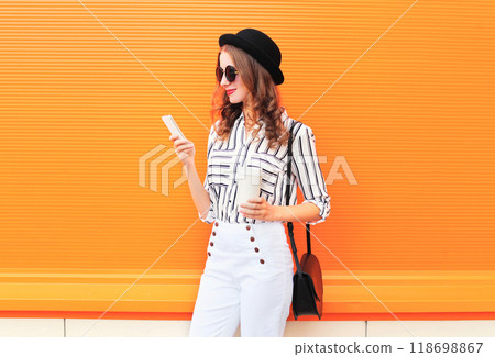 Fashion pretty young woman model using smartphone with coffee cup on colorful orange background 118698867