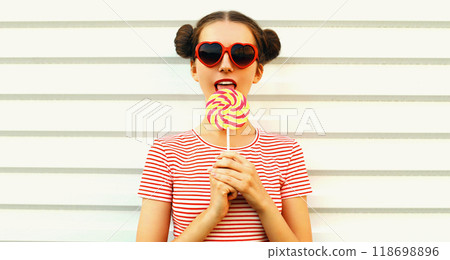 Summer portrait of happy young woman licks lollipop on white background 118698896