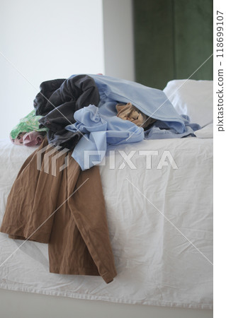 A disorganized and messy pile of various clothes scattered on a bed in the bedroom A disorganized and messy pile of various clothes scattered on a bed in the bedroom 118699107