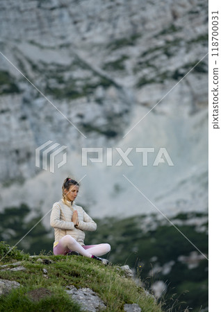 Young woman meditating in lotus position surrounded by mountains 118700031