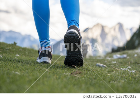 Low angle view of female legs in hiking shoes walking on green grass 118700032