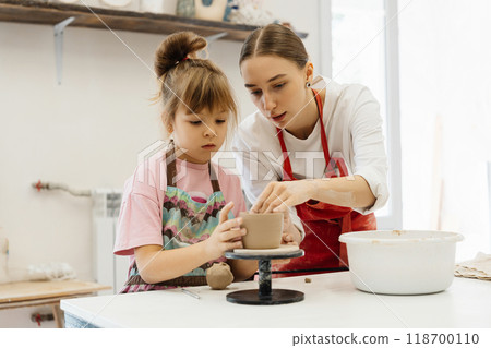 Mother and daughter create pottery together in a bright studio 118700110