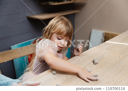 Girl plays with clay at a wooden table in an art studio setting Girl plays with clay at a wooden table in an art studio setting 118700118