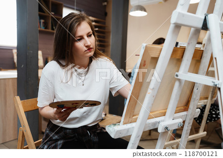 Young artist painting on easel in a creative studio during afternoon session 118700121
