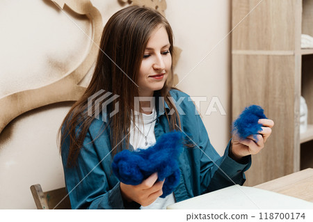 A woman engages in creative textile art by manipulating blue fibers indoors A woman engages in creative textile art by manipulating blue fibers indoors 118700174