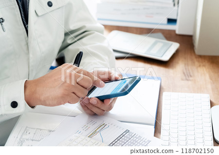 一個穿著工作服的男人操作智慧型手機的手 118702150