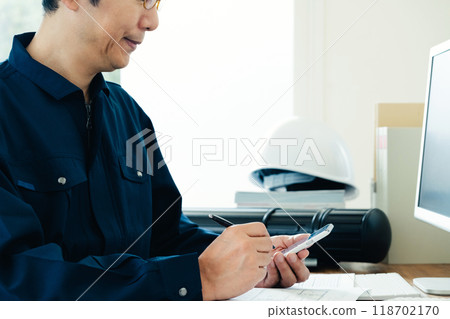 Man in work clothes operating a smartphone Man in work clothes operating a smartphone 118702170