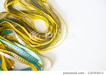 A lot of multi-colored centimeter and inch measuring tapes lie on a white background on the table. A lot of multi-colored centimeter and inch measuring tapes lie on a white background on the table. 118703013
