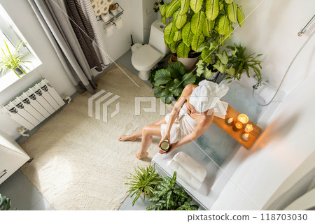 A young, beautiful woman sits on the edge of a bubble bath and applies moisturizer to her skin. A young, beautiful woman sits on the edge of a bubble bath and applies moisturizer to her skin. 118703030