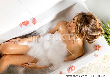 A young, beautiful and sexy girl takes a bath with foam and rose petals. The concept of pleasure 118703043