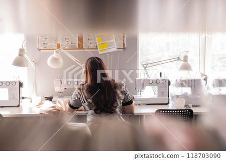 Woman plus size fashion designer uses a sewing machine in her studio. Woman plus size fashion designer uses a sewing machine in her studio. 118703090