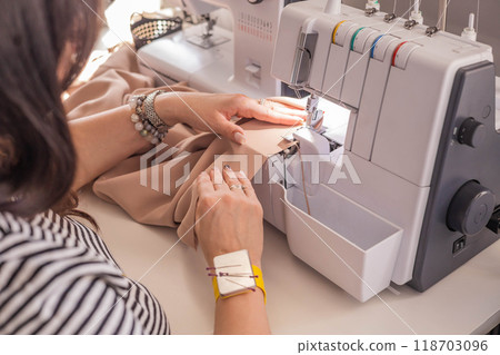 A plus size woman fashion designer uses an overlock sewing machine in her studio.  118703096