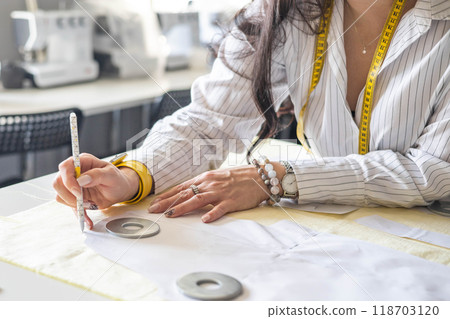 Beautiful young woman plus size dressmaker lays out pattern details on denim and cuts clothes Beautiful young woman plus size dressmaker lays out pattern details on denim and cuts clothes 118703120