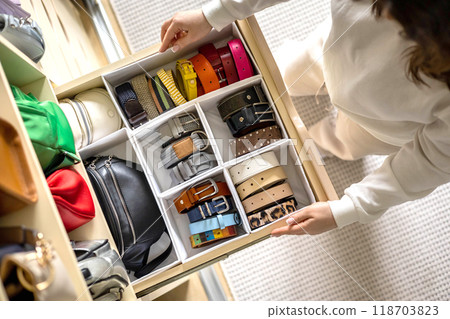 A young beautiful woman puts a convenient order in storing belts in her home wardrobe. A young beautiful woman puts a convenient order in storing belts in her home wardrobe. 118703823