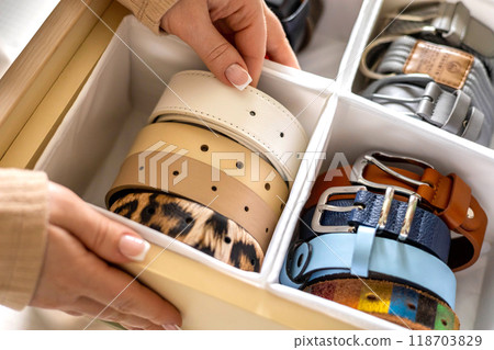 A woman chooses a matching belt. Lots of belts neatly stacked in a wardrobe drawer. A woman chooses a matching belt. Lots of belts neatly stacked in a wardrobe drawer. 118703829
