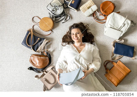 A young beautiful girl lies on the floor in the dressing room, surrounded in a circle by fashionable 118703854