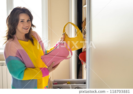 A happy, smiling, beautiful woman chooses a fashionable bag for herself in her home wardrobe.  118703881