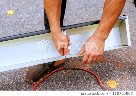 Worker attaches concealed gutter hangers to new gutters before attaching them to roof using pre installed screws 118703907