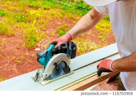 Working with circular handsaw, worker cuts plastic vinyl siding to required size before installing it Working with circular handsaw, worker cuts plastic vinyl siding to required size before installing it 118703908