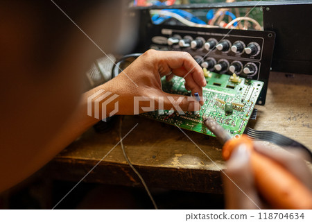 Repairman using soldering iron installs capacitor on printed circuit board at workbench 118704634