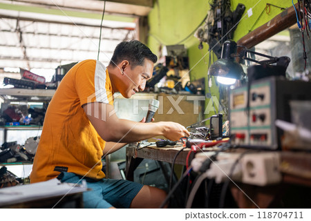 Asian male technician fixes broken cable in electronics repair room Asian male technician fixes broken cable in electronics repair room 118704711