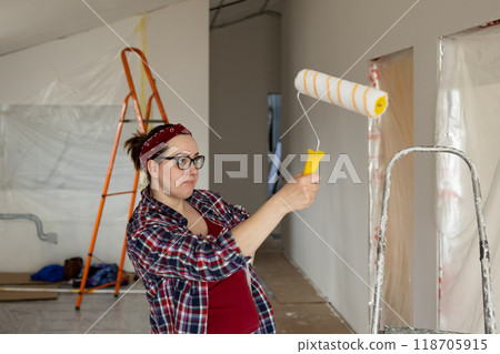A woman is painting the interior of her house using a roller during a home renovation project A woman is painting the interior of her house using a roller during a home renovation project 118705915