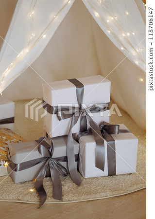 Christmas interior. White wigwam illuminated with lights, and gifts are stacked inside. Christmas interior. White wigwam illuminated with lights, and gifts are stacked inside. 118706147
