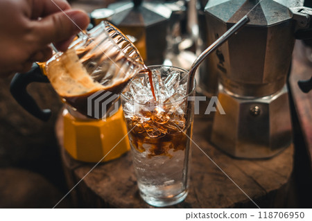 Making iced coffee. Pouring coffee into a glass with ice. 118706950