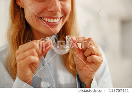 A Smiling Woman Proudly Holding Clear Dental Aligners that Help Achieve a Perfect Smile 118707321