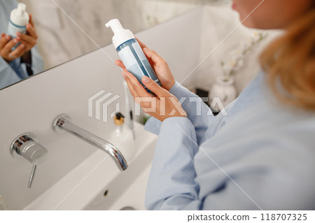 A woman applying skincare foam while in a beautifully designed modern bathroom setting 118707325